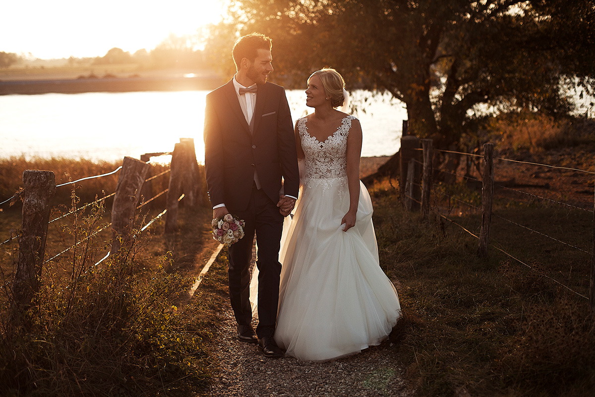 Hochzeitsfotografie Brautpaar beim Spaziergang am Wasser mit einer untergehenden Sonne