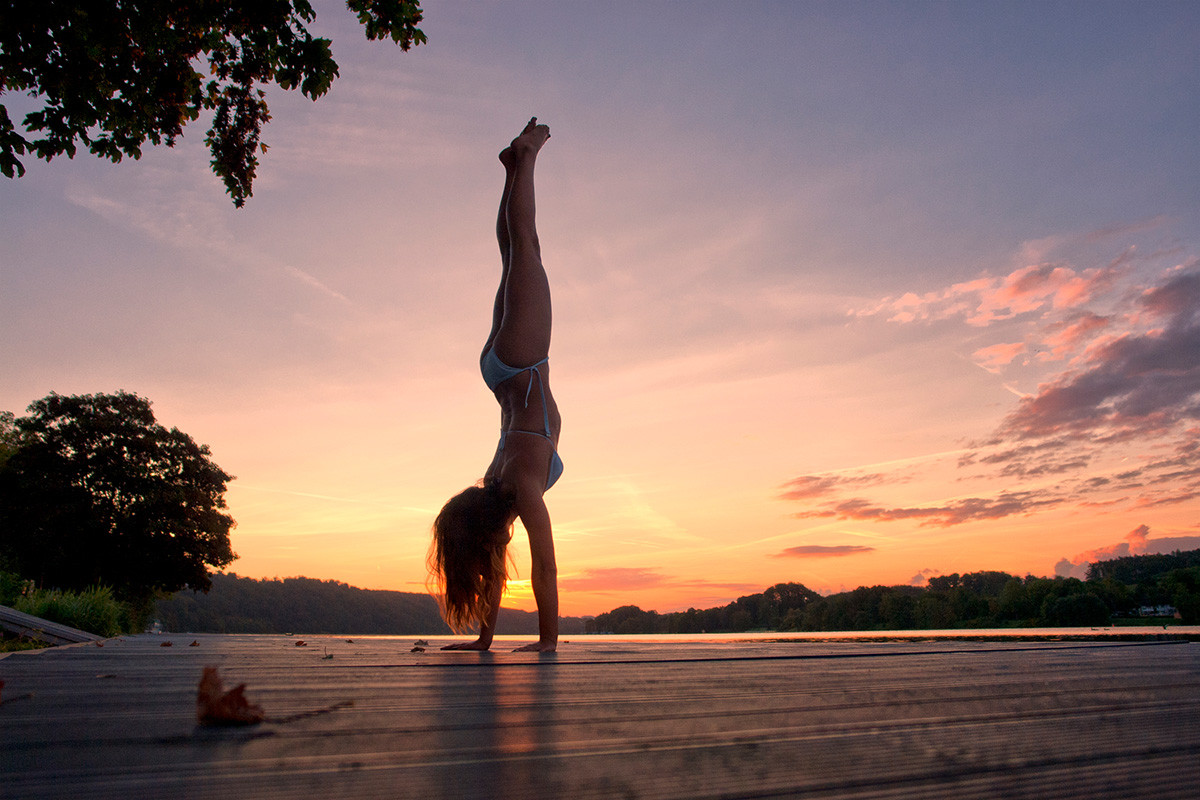 Outdoorfotografie weibliche Person macht einen Handstand am Steg beim Sonnenaufgang