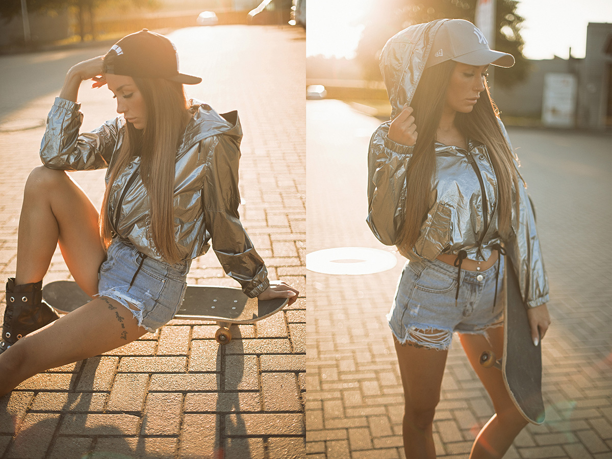 Outdoorfotografie weibliche Person mit Silberne Hoodie Jacke, Base Cap, Hot Pants und Skateboard. Die Sonne geht im Hintergrund unter.