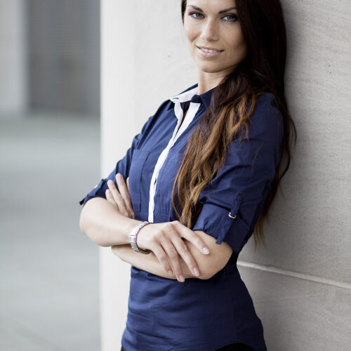 Lifestyle-Business: Frau in blauer Bluse lehnt an einer Wand im modernen Büro.