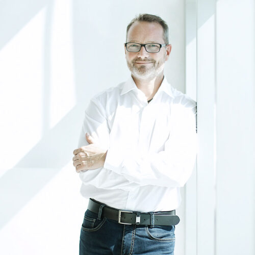 Businessfotografie Essen: Seriöser Geschäftsmann in weißem Hemd und Brille vor hellem Hintergrund.