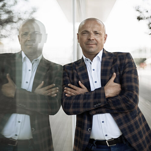 Unternehmensfotografie männliche Person im Außenbereich mit Sakko und Hemd vor einer Fensterfront