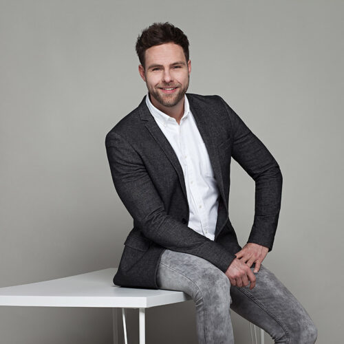 Business-Shooting: Unternehmer sitzt entspannt auf einem Tisch für ein modernes Portrait.