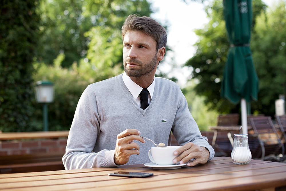 Werbefotografie männliche Person im Lacoste Oberteil in einem Cafe in der Natur