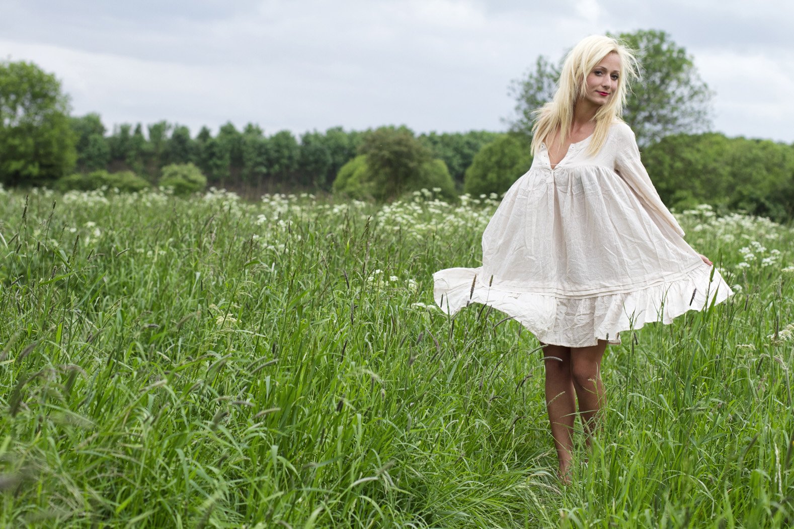 Werbefotografie weibliche Person mit blonden Haaren in einem weissen Kleid. Sie steht auf einer Wiese.